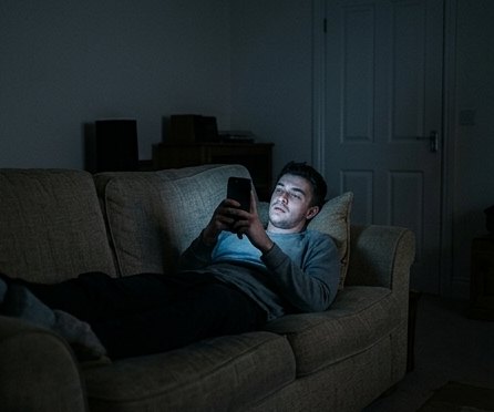 Screen addiction at night, doomscrolling on a sofa in the dark
